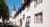Historisches Gebäude mit weißen Wänden, roten Fensterrahmen und einem Kirchturm im Hintergrund.