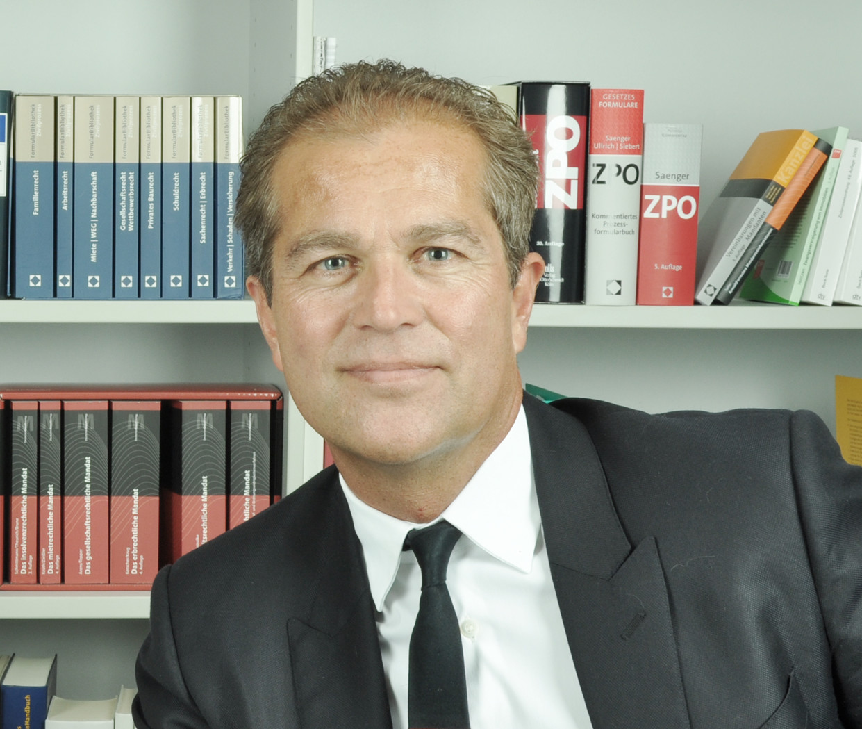 Zwei Personen vor Bücherregal, eine Frau und ein Mann, professionell gekleidet.