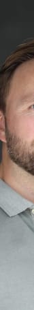 Porträt eines Mannes mit braunem Haar und Bart vor dunklem Hintergrund.