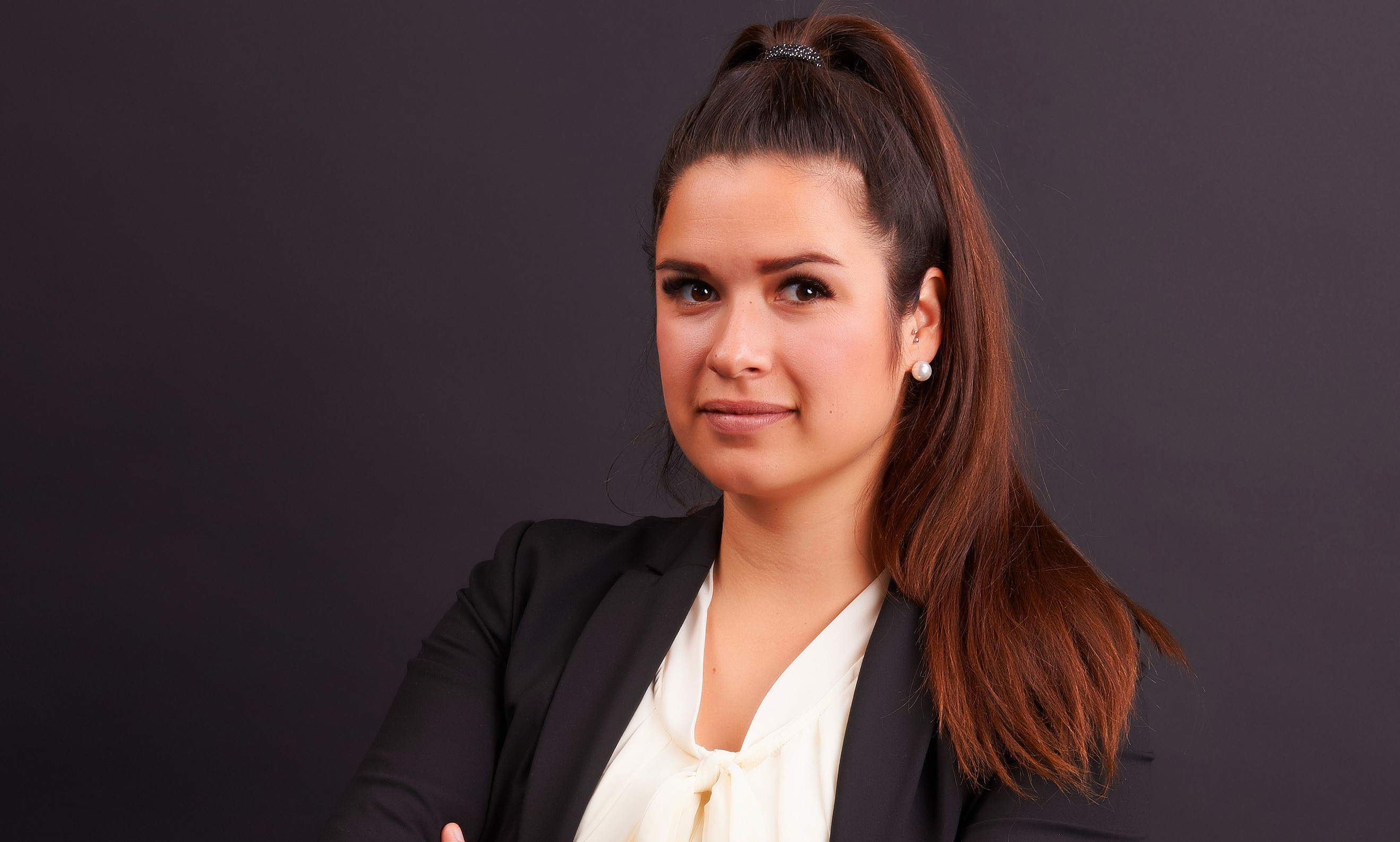 Selbstbewusste Geschäftsfrau mit verschränkten Armen vor dunklem Hintergrund.