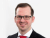 Ein Mann mit Brille, Anzug und roter Krawatte lächelt in die Kamera.