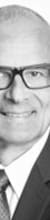 Porträt eines Mannes in formeller Kleidung mit Brille, lächelnd, in Schwarz-Weiß.