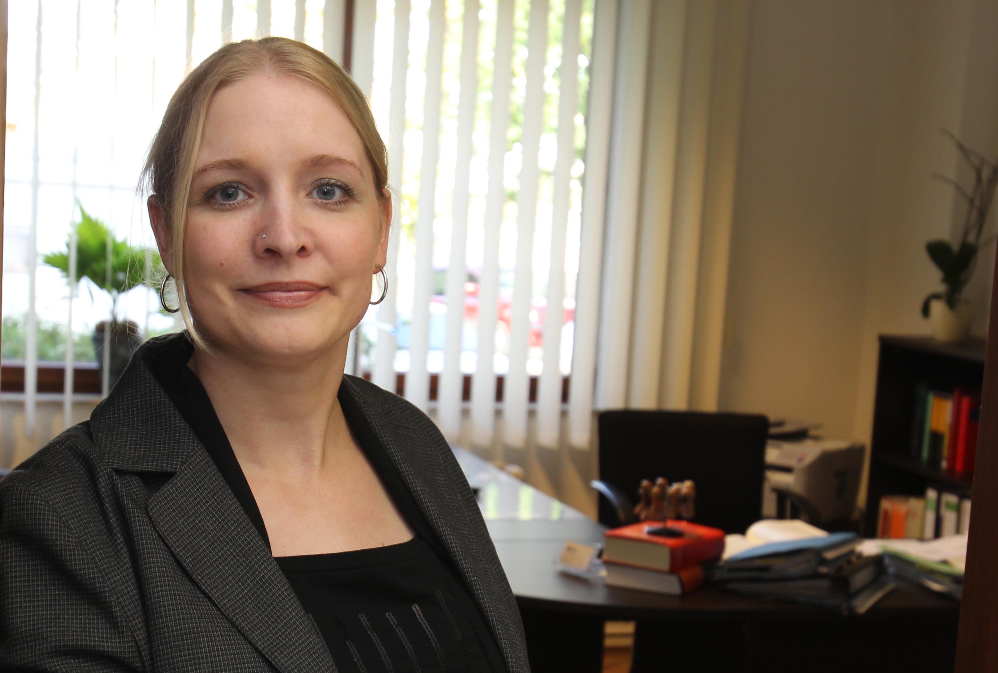 Frau mit blonden Haaren hält einen offenen Aktenordner in einem Büro.