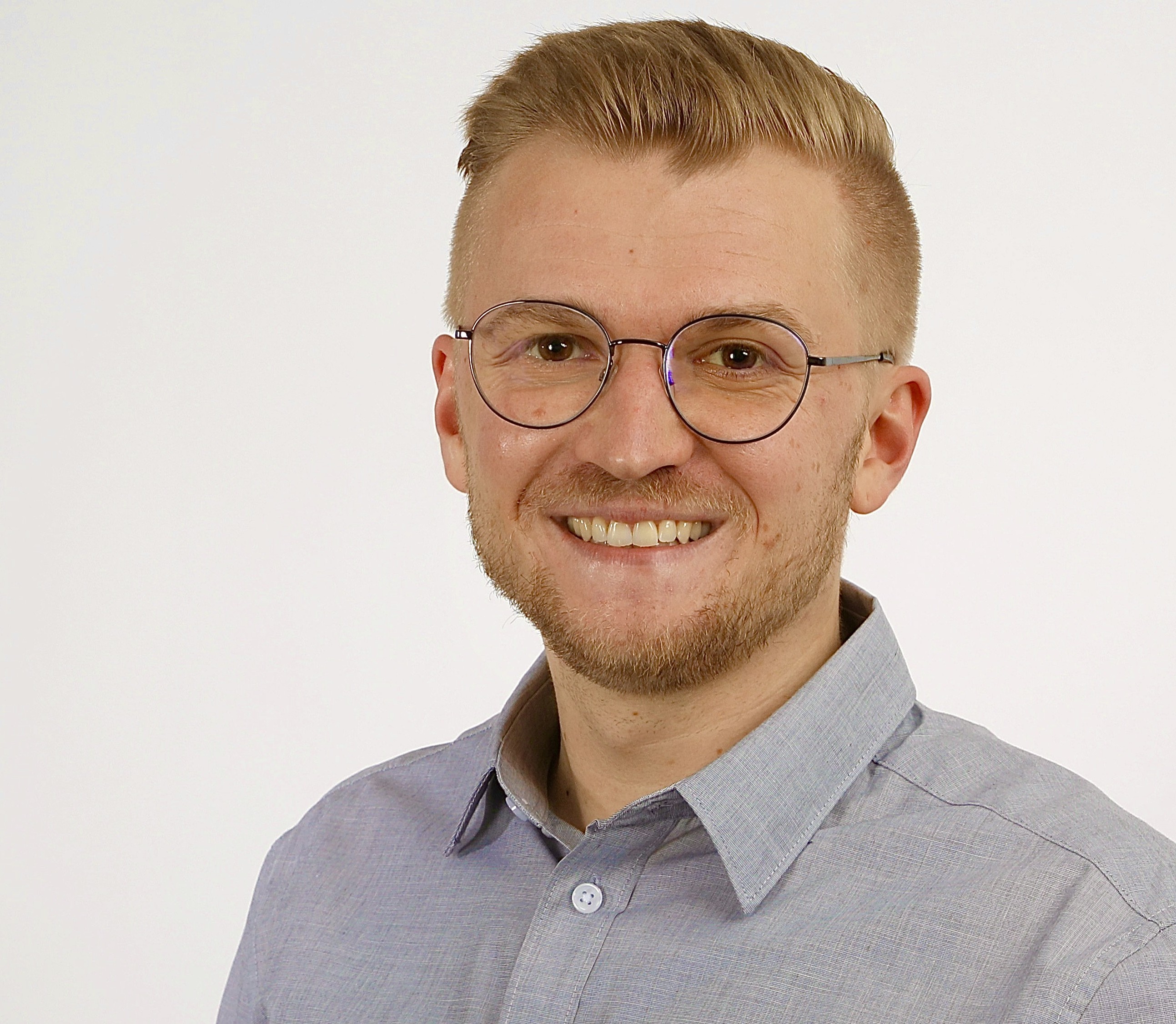 Ein Mann mit Brille und Bart hält ein Tablet in den Händen und lächelt.