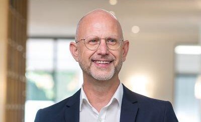 Lächelnder Mann in formeller Kleidung vor hellem, modernem Hintergrund.