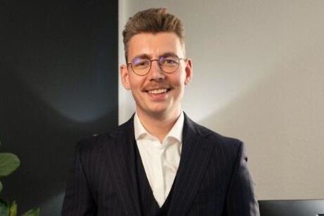 Lächelnder Mann in Anzug vor einem Bürohintergrund.
