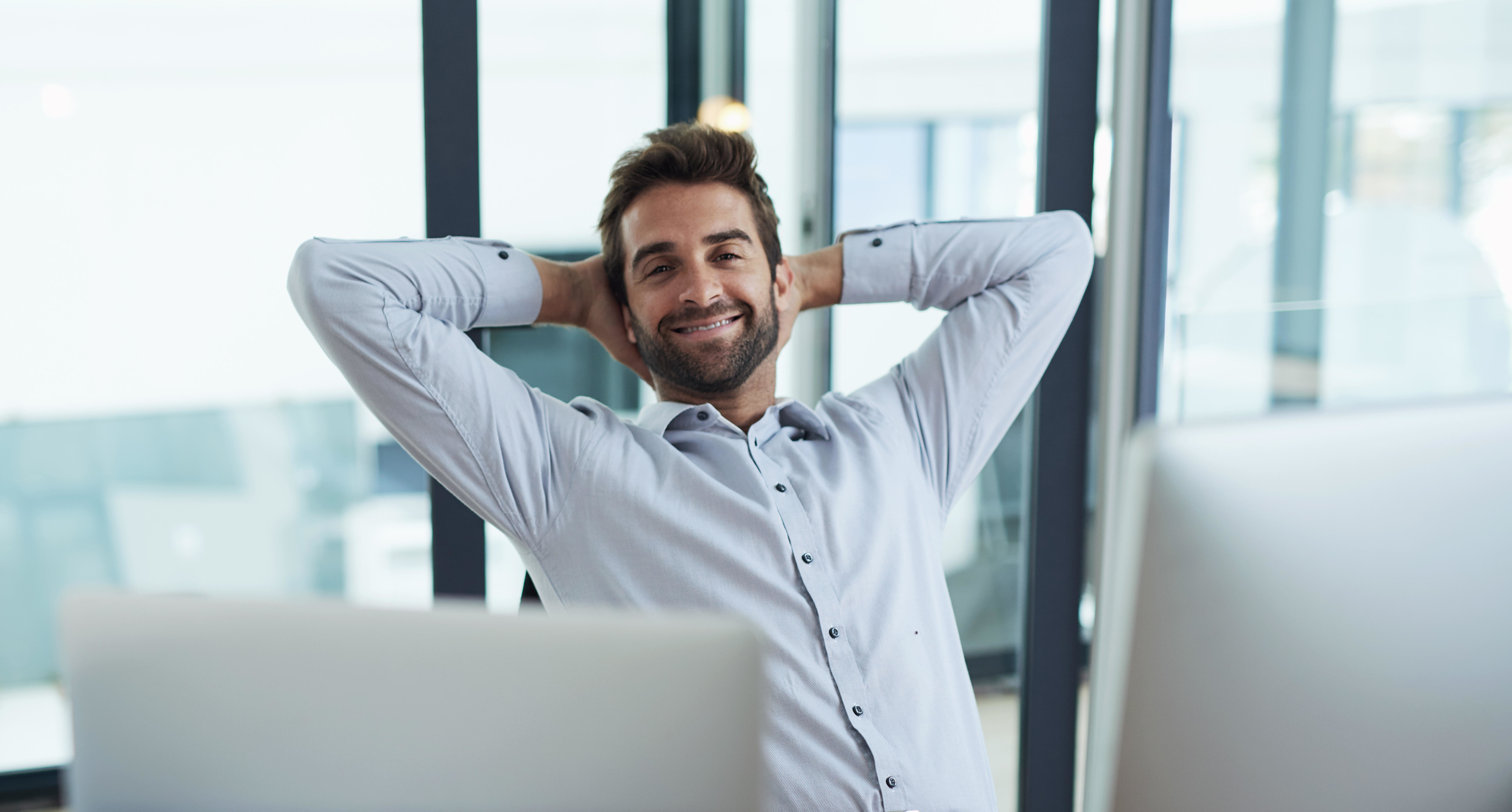 Lächelnder Mann sitzt entspannt im Büro mit Laptop und Kaffeetasse.