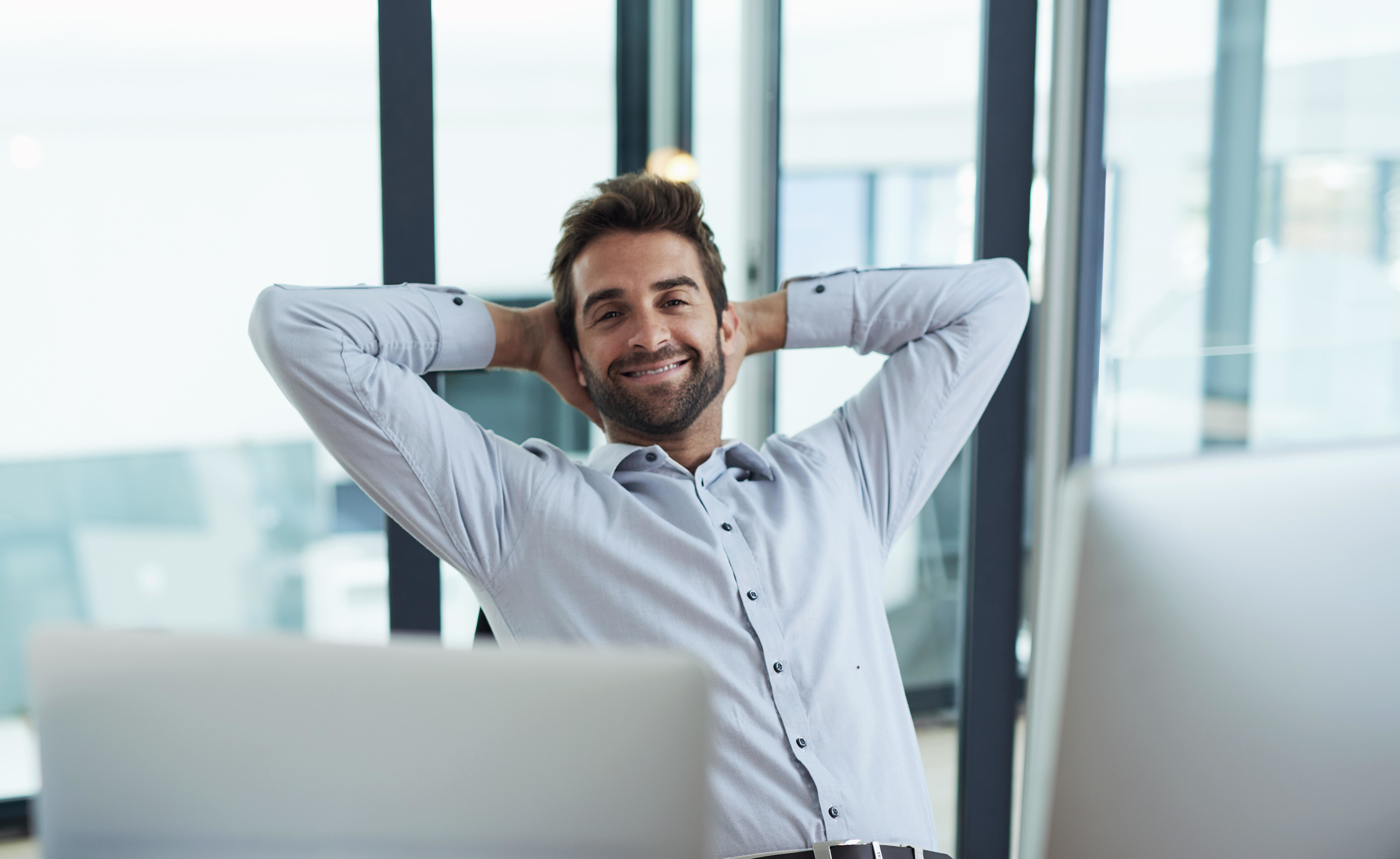 Lächelnder Mann sitzt entspannt im Büro mit Laptop und Kaffeetasse.
