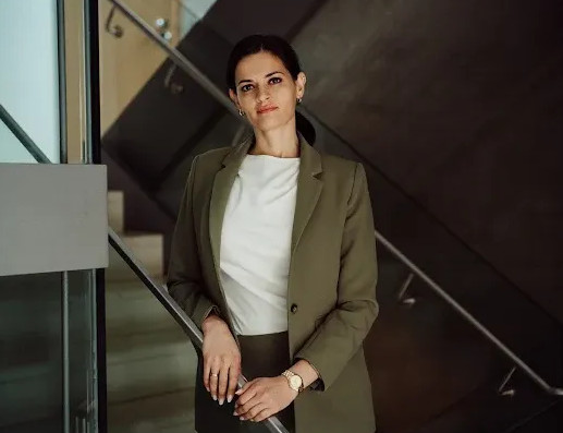 Frau in Businesskleidung steht an einer Treppe in einem modernen Gebäude.