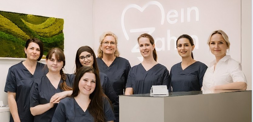 Zahnärztliches Team in Praxis mit "Mein Zahn" Logo im Hintergrund.