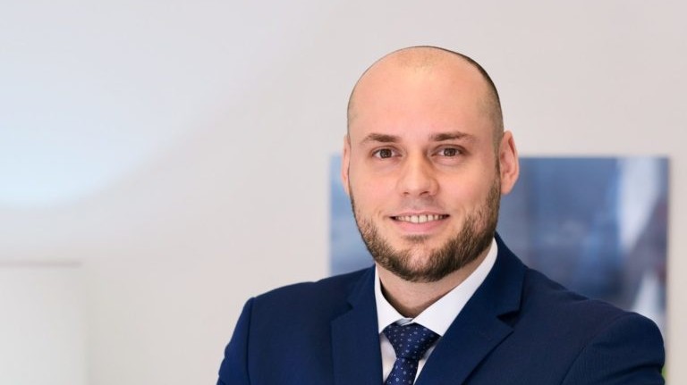 Geschäftsmann in Anzug mit verschränkten Armen vor neutralem Hintergrund.