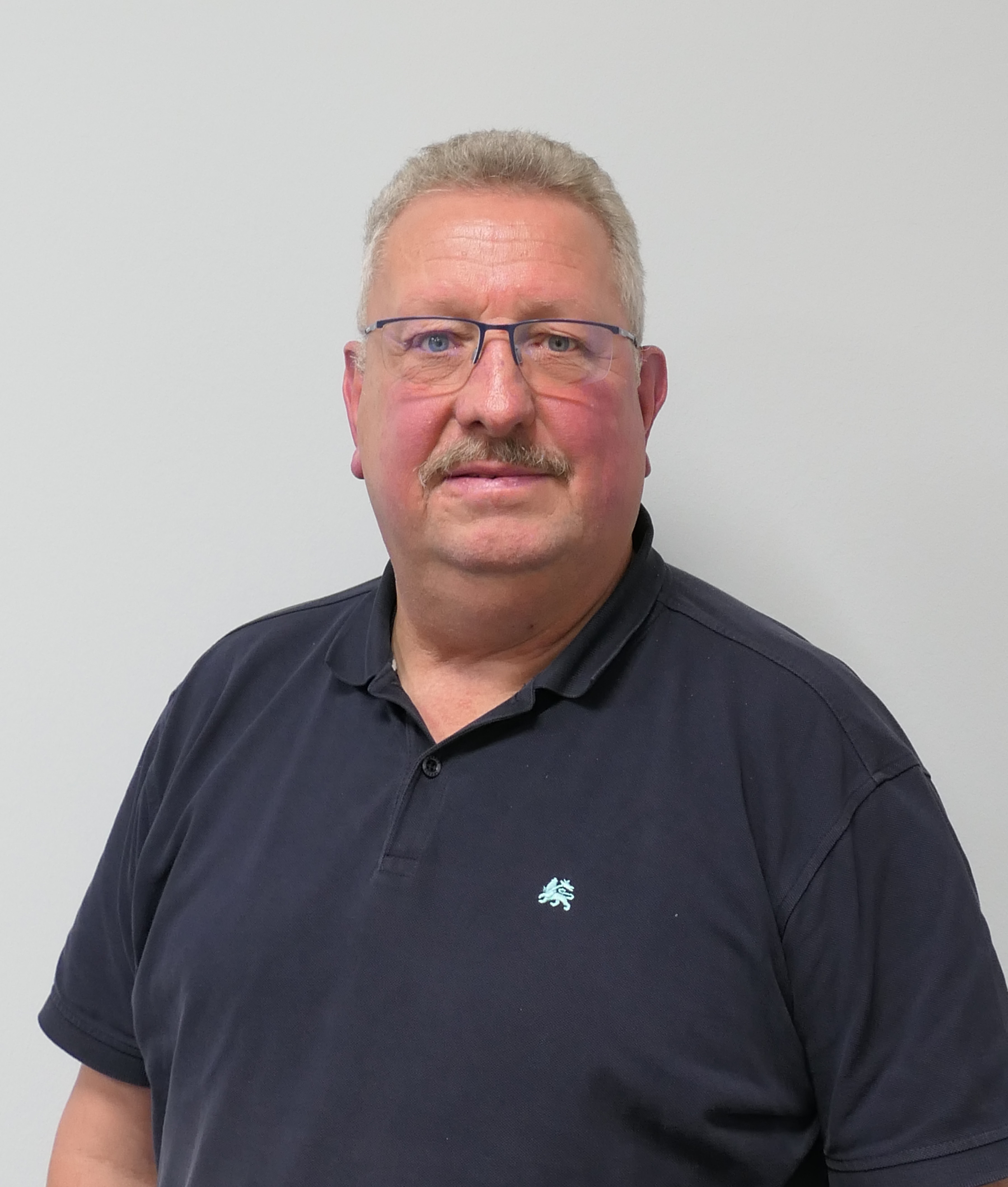 Porträt eines Mannes mit Brille vor weißer Wand.