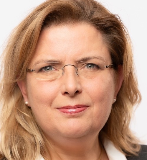 Porträt einer Frau mit Brille, blonden Haaren und einem weißen Hemd.