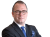 Ein Mann in einem schwarzen Anzug mit Brille, blauer Krawatte und Armbanduhr, der die Arme verschränkt.