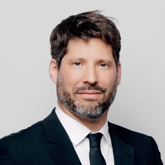 Porträt eines Mannes in formeller schwarzer Anzug mit Krawatte vor hellem Hintergrund.