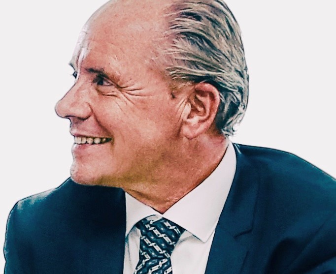 Lächelnder Mann in Anzug und Krawatte, seitlich betrachtet.