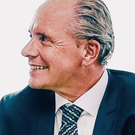 Lächelnder Mann in Anzug und Krawatte, seitlich betrachtet.