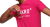 Junger Mann in pinkem T-Shirt mit weißen Aufdruck, lächelnd und in einer entspannten Pose.