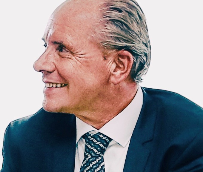 Lächelnder Mann in Anzug und Krawatte, seitlich betrachtet.