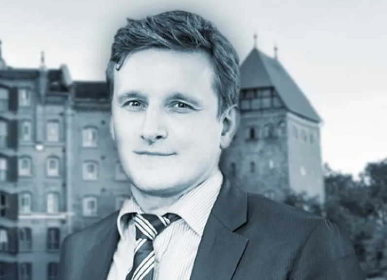 Ein Mann in formeller Kleidung vor einem historischen Gebäude.