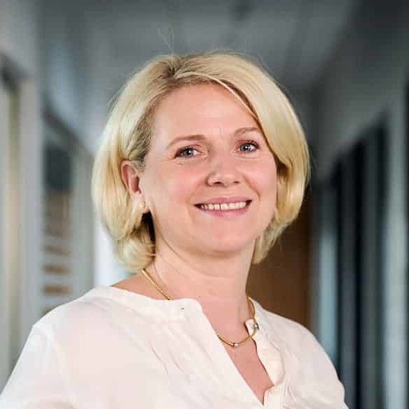 Lächelnde Frau in einem Flur mit Kunstwerken an der Wand und Schließfächern.