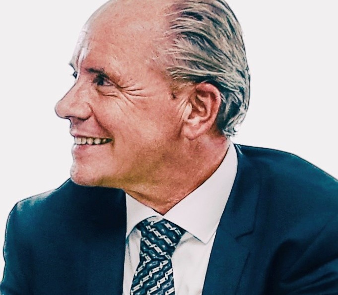 Lächelnder Mann in Anzug und Krawatte, seitlich betrachtet.