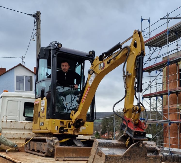 Kleiner Bagger auf einem Bauwagen, bereit für den Einsatz auf einer Baustelle.