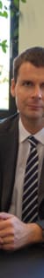 Geschäftsmann sitzt an seinem Schreibtisch im Büro, umgeben von Büromaterialien und Computern.