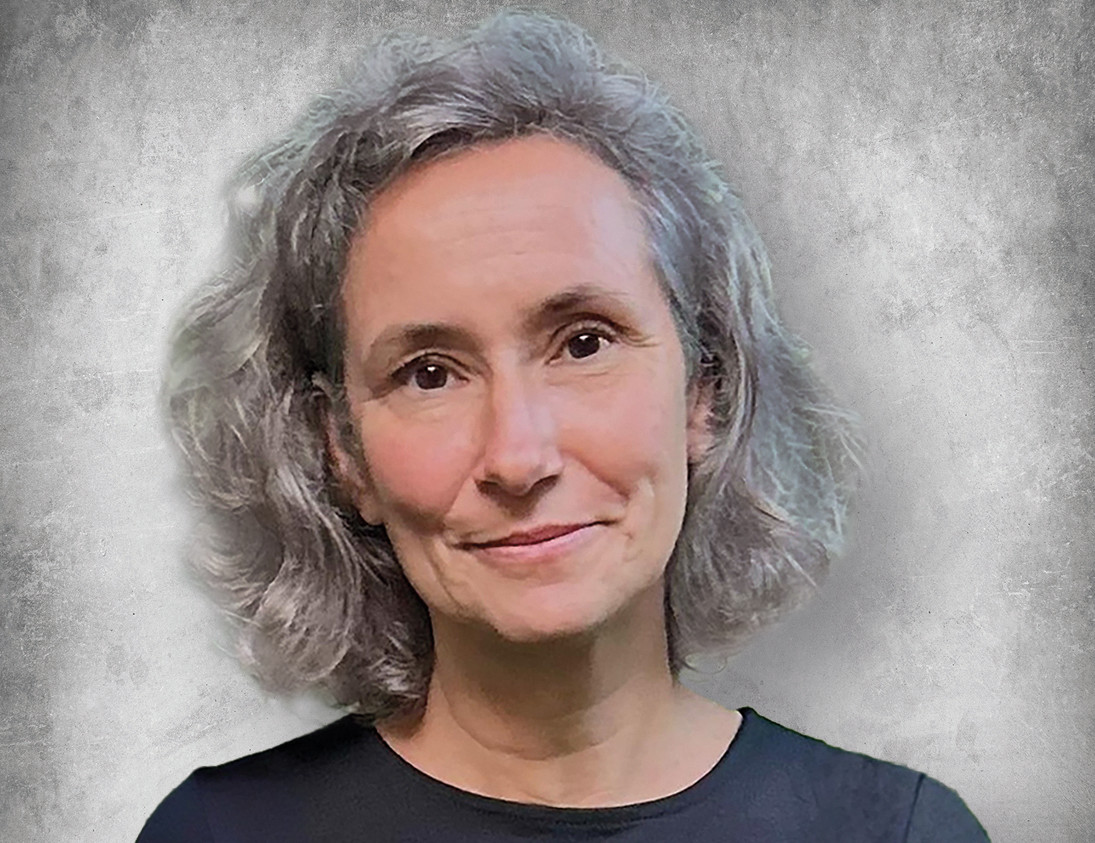 Porträt einer Frau mit grauem, lockigem Haar vor einem grauen Hintergrund.