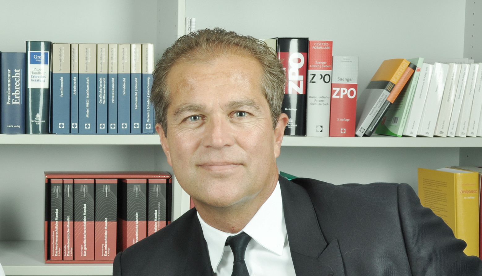 Zwei Personen vor Bücherregal, eine Frau und ein Mann, professionell gekleidet.