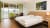Doppelbettzimmer mit Holzfußboden, Wandlampe, Wandbild eines Wasserfalls, Kreuz an der Wand, Balkon mit Blick auf Berge, Tisch mit Stuhl und Pflanze.