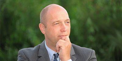 Ein Mann in einem Anzug, der nachdenklich nach oben schaut, im Grünen.
