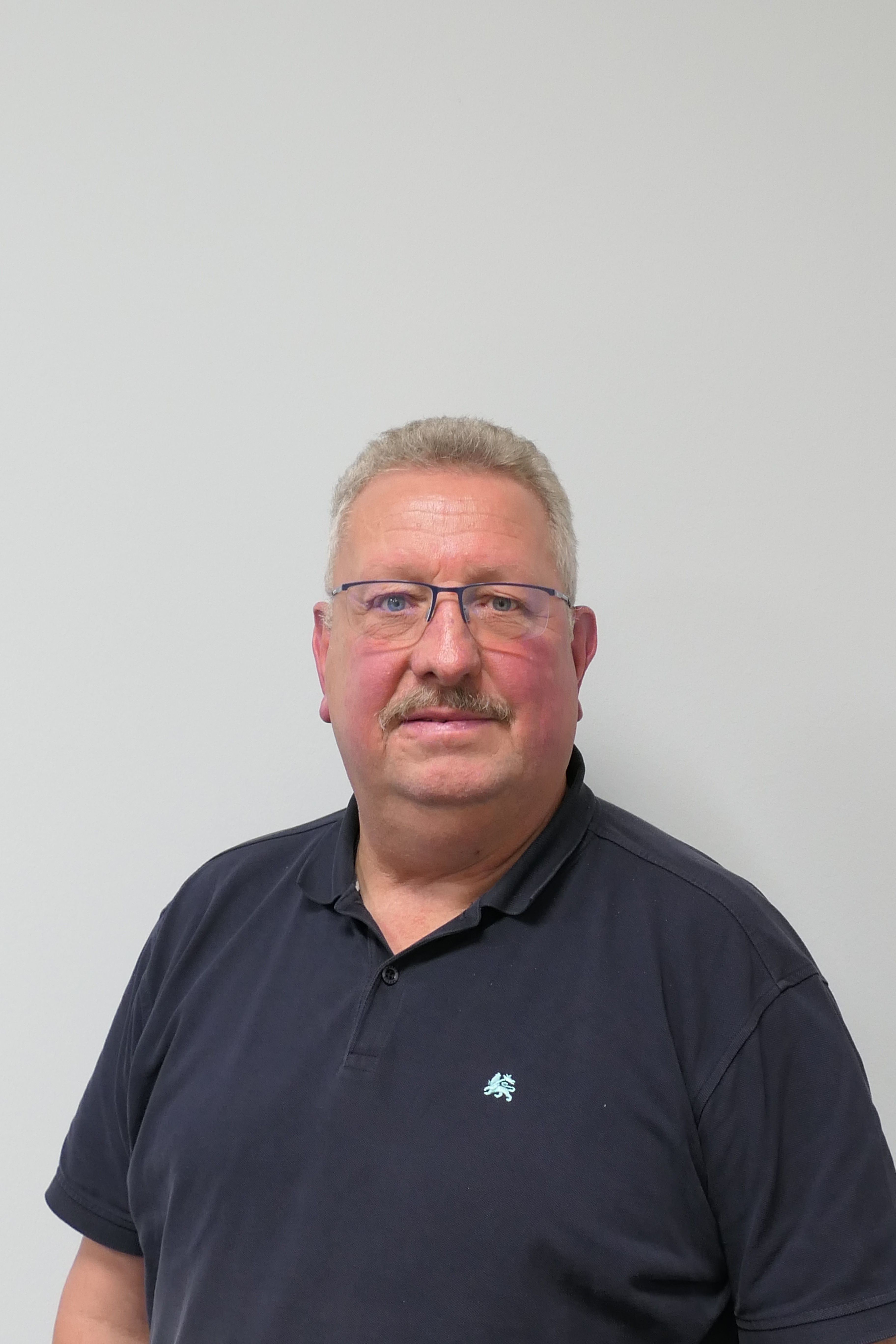 Porträt eines Mannes mit Brille vor weißer Wand.