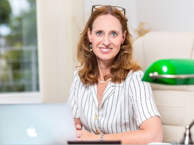 Eine Frau sitzt an einem Schreibtisch mit einem Laptop und lächelt.