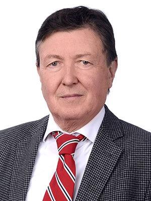 Porträt eines älteren Mannes in Anzug und roter Krawatte.