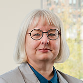 Ältere Frau mit Brille und weißen Haaren, im Büro mit Fenster im Hintergrund