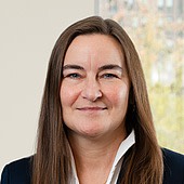 Ein Porträt einer Frau mit braunen Haaren, die freundlich in die Kamera lächelt.