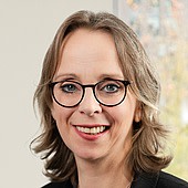 Ein Porträt einer Frau mit Brille, die lächelnd in die Kamera schaut.