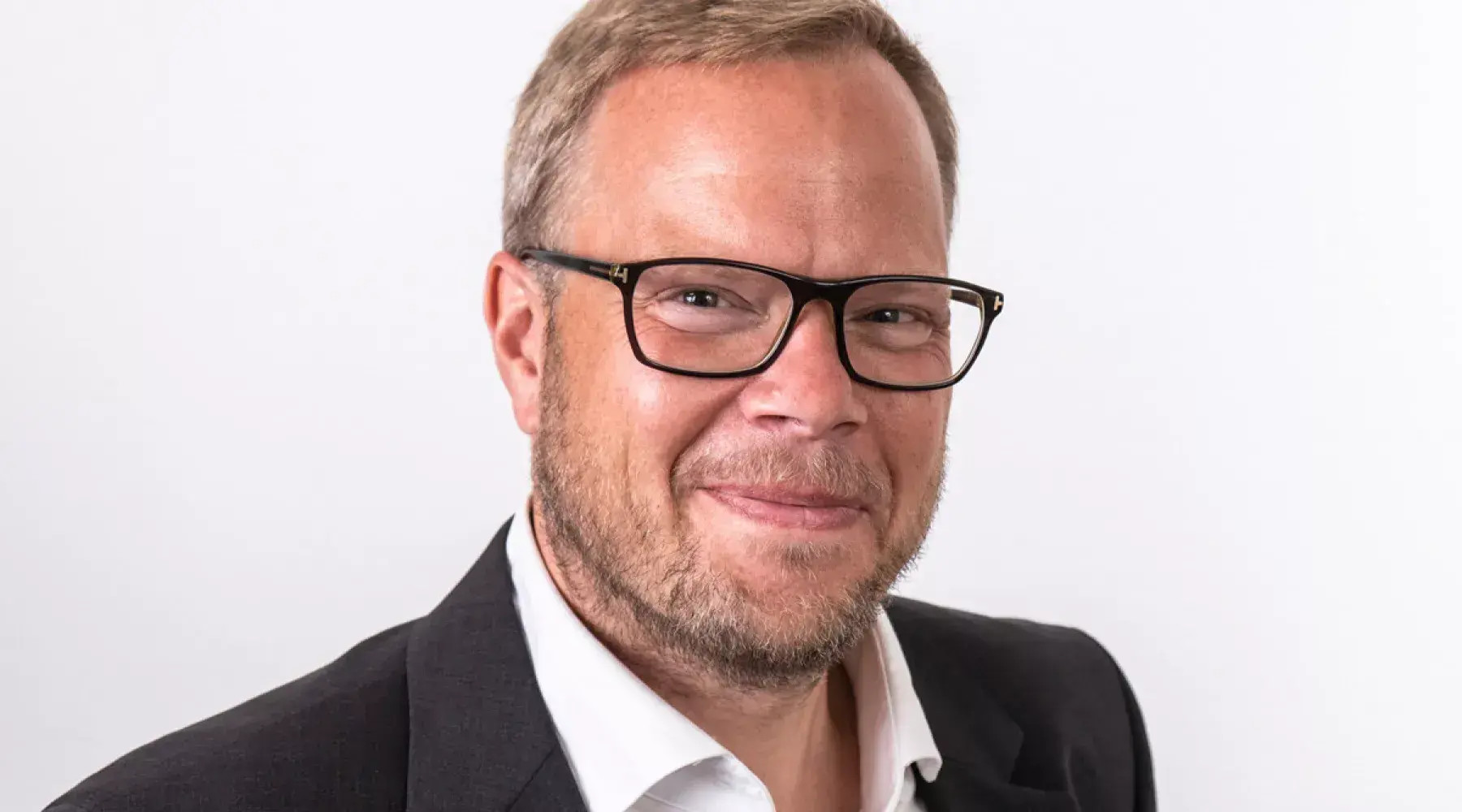 Porträt eines Mannes mit Brille, Anzug und weißem Hemd vor weißem Hintergrund.