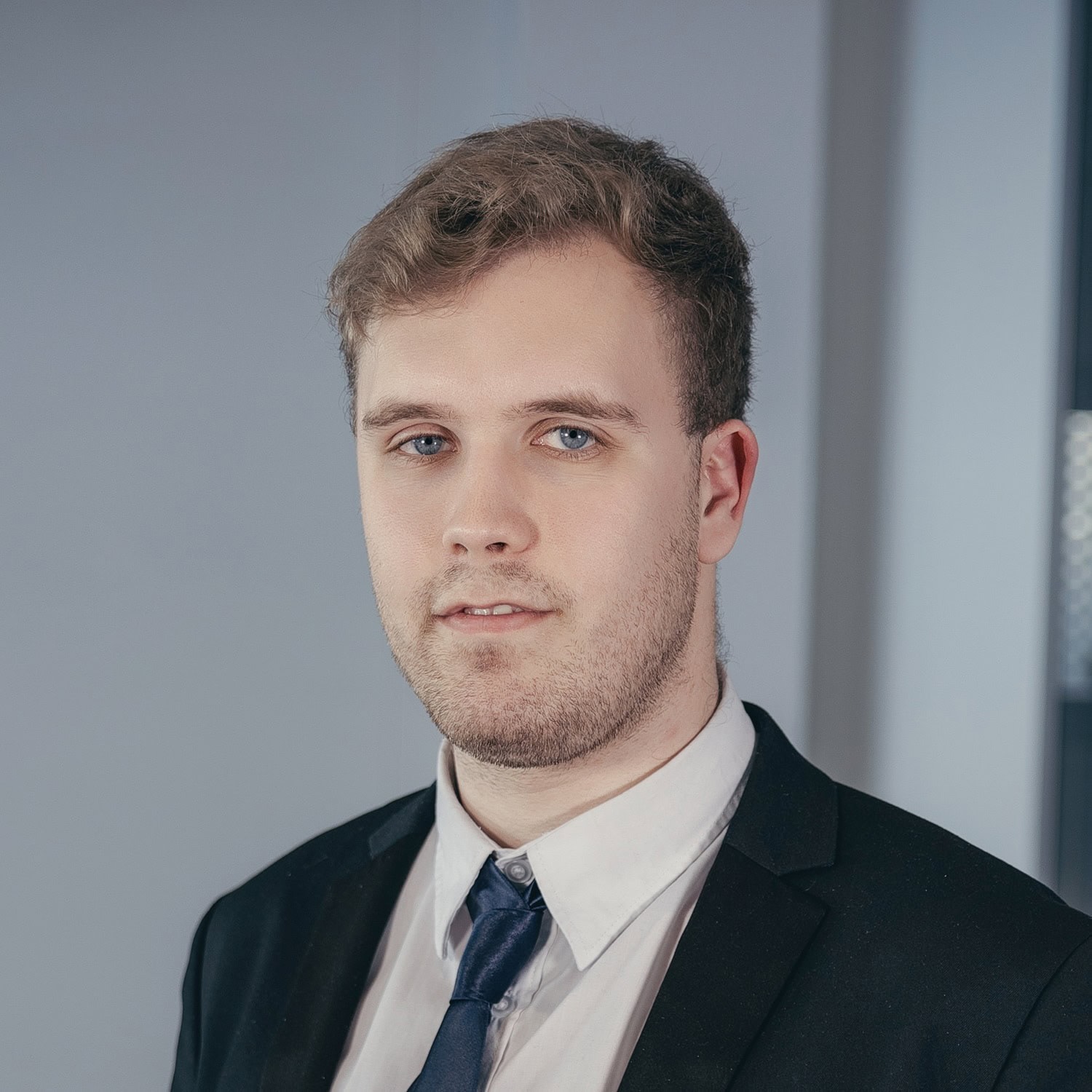 Porträt eines jungen Mannes in formeller Kleidung vor einem neutralen Hintergrund.
