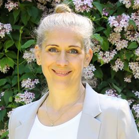 Frau mit grauem Haar vor blühendem Busch