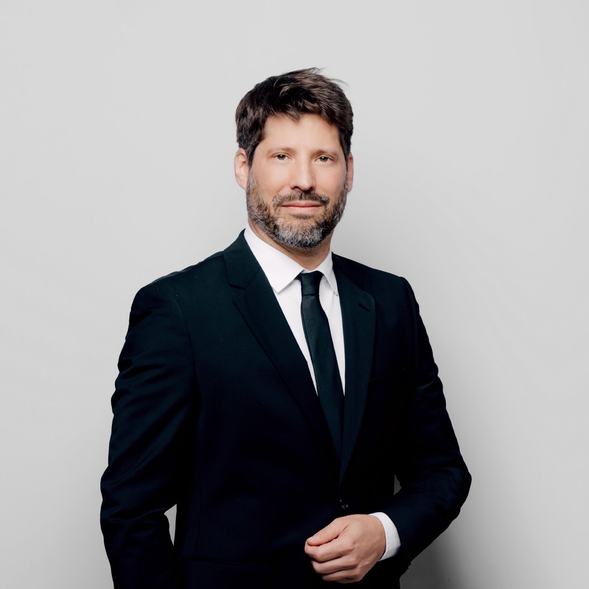 Porträt eines Mannes in formeller schwarzer Anzug mit Krawatte vor hellem Hintergrund.