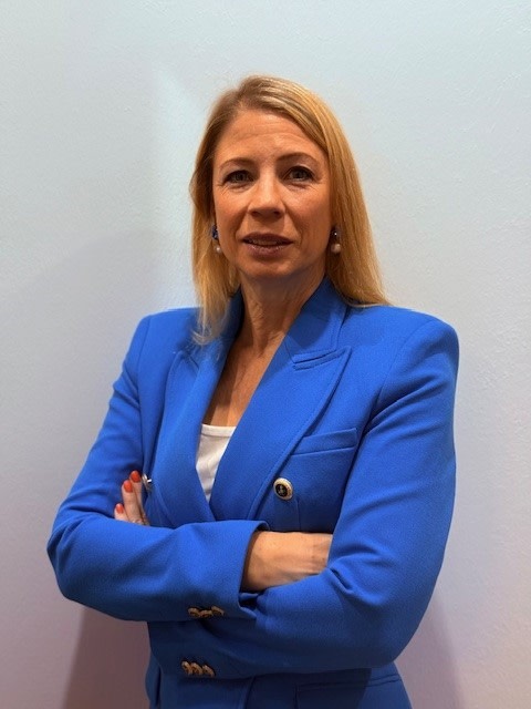 Frau in blauer Blazer mit verschränkten Armen vor hellem Hintergrund.