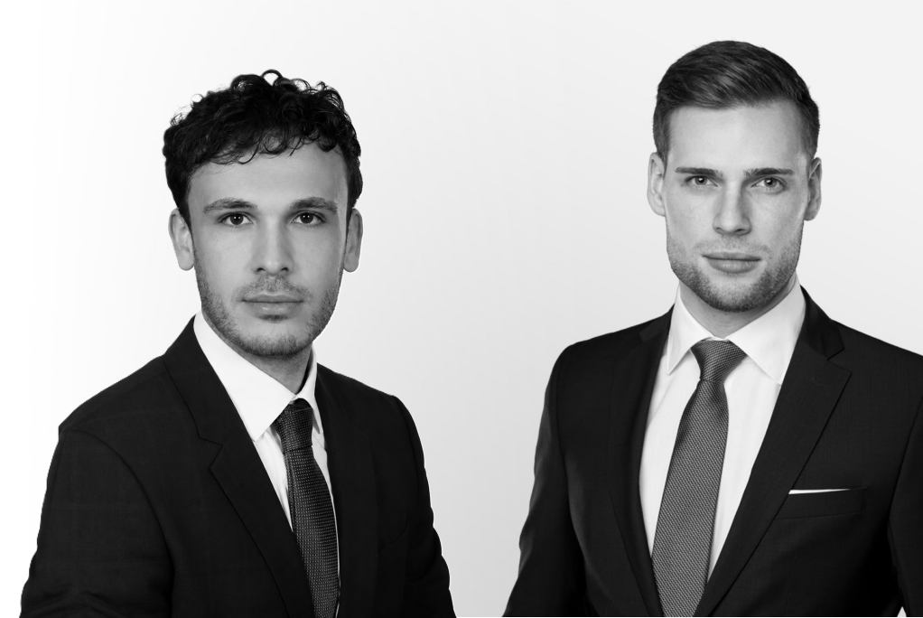 Zwei junge Männer in formellen Anzügen, die in die Kamera schauen.