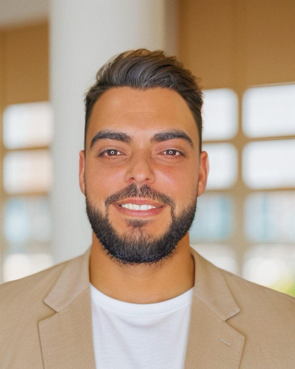 Lächelnder Mann in Business-Kleidung vor einem hellen, modernen Hintergrund.