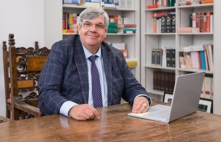 Geschäftsmann sitzt an einem Schreibtisch mit einem Laptop, umgeben von Bücherregalen.