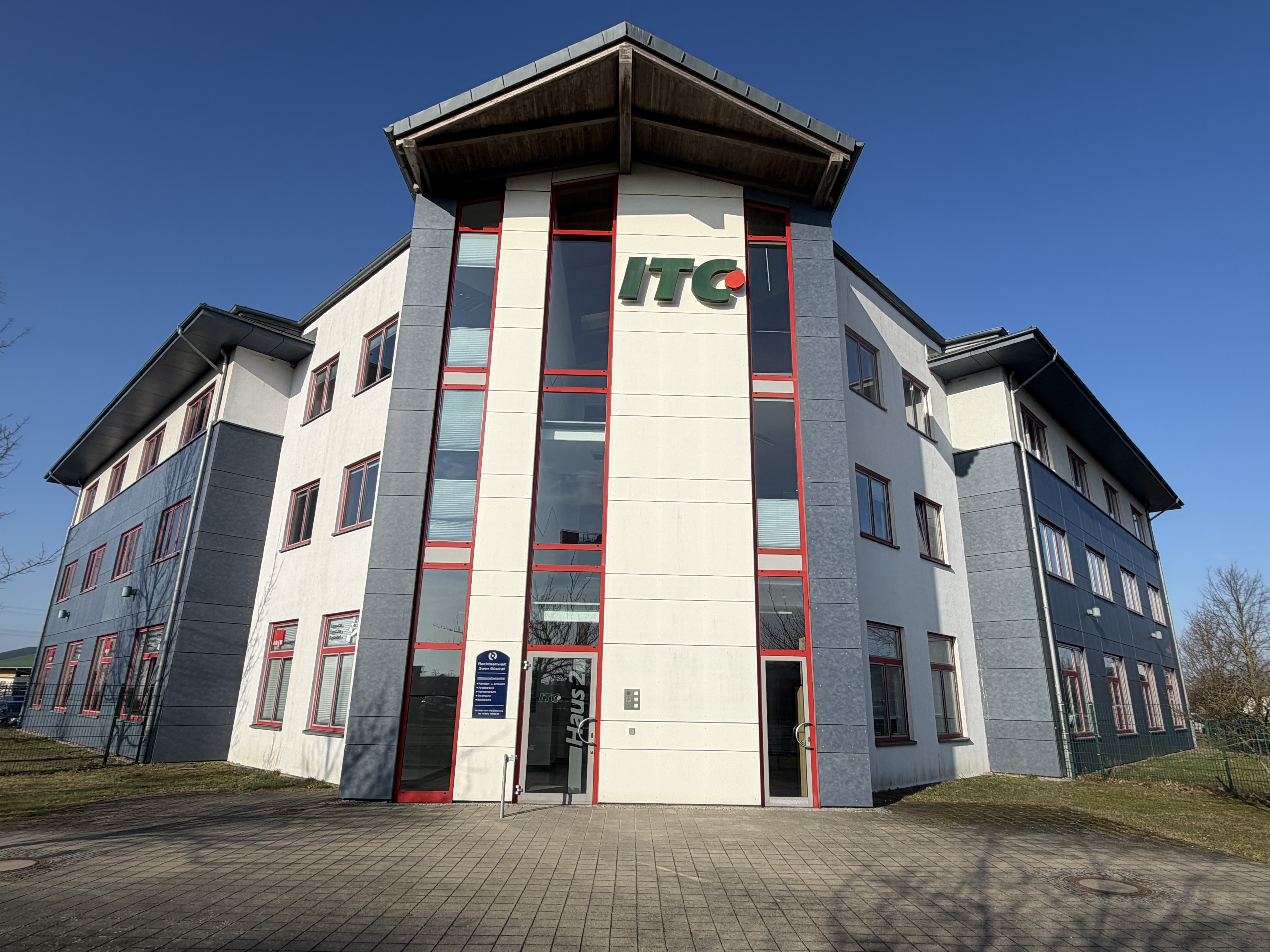 Mehrstöckiges Bürogebäude mit weißen und grauen Fassaden, rote Fensterrahmen und ein grünes und rotes "ITC" Logo an der Front.