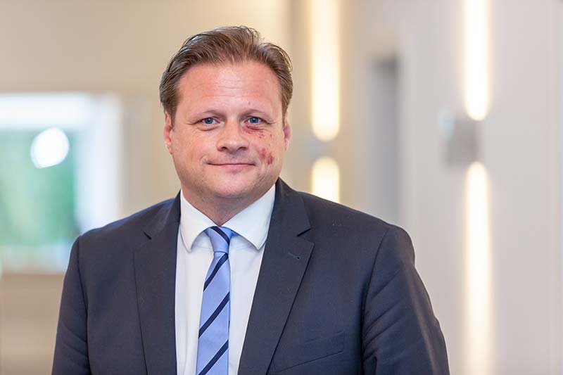 Geschäftsmann in Anzug mit leichten Verletzungen im Gesicht, lächelnd in einem modernen Büro.