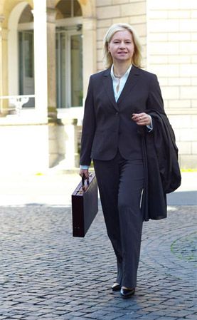 Frau in Businesskleidung mit Aktenkoffer und Mantel, die auf der Straße geht.
