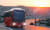 Ein moderner Reisebus fährt auf einer kurvigen Straße durch eine Wüstenlandschaft bei Sonnenuntergang.